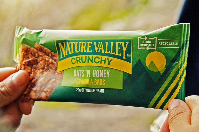 Two hands holding an individually wrapped Nature Valley Oats 'N Honey Granola Bar.