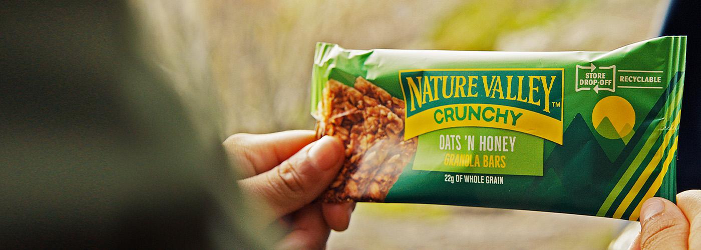 Two hands holding an individually wrapped Nature Valley Oats 'N Honey Granola Bar.